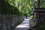 A path through a wooded area next to a wall of unhewn stones.