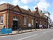 A red-and-brown bricked building with a rectangular, dark blue sign reading "UPTON PARK STATION" in white letters all under a light blue sky