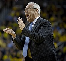 A man with short gray hair wearing a suit claps his hands.