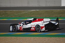 A side view of the Toyota TS050 Hybrid Le Mans Prototype 1 racing car with the number 7 inside a red triangle painted to the right of the front-left wheel