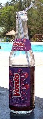 a bottle of Vimto with a straw placed on a table near a swimming pool on a sunny day