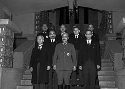 photo de groupe des ministres. Une douzaine d'hommes debout en uniformes sont rassemblés en bas d'un large escalier ; au centre, en uniforme militaire, se tient le premier ministre.