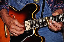 A musician playing a slide guitar with a slide on their little finger