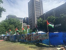 A tall fence obstructed by blue tarp and covered in signs and Palestinian flags