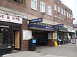 A brown-bricked building with a rectangular, dark blue sign reading "QUEENSBURY STATION" in white letters all under a light blue sky