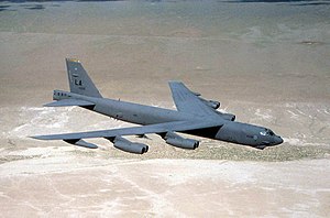 Aerial top/side view of gray B-52 overflying barren land.