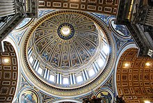 Photo looking up at the dome's interior from below. The dome is decorated at the top with a band of script. Around its base are windows through which the light streams. The decoration is divided by many vertical ribs which are ornamented with golden stars.