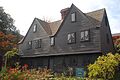 A brown-painted colonial house with two large front-facing gable dormers. The windows have very small diamond panes of glass.