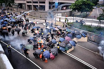 Protesters with umbrellas are being dispersed by tear gas.