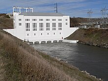 Powerhouse with tailrace canal running out of base; electrical transformers on canal bank at right