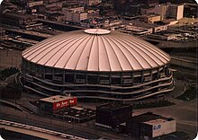 Aerial view of a domed stadium with a large roof topped by an American flag.