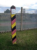 The third-generation fence, constructed from several overlapping horizontal tiers of expanded steel mesh fencing. A border marker pole is in the foreground.