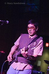 A man in sunglasses onstage performs on an electric guitar.