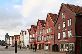 Foto von alten Holzhäusern, die dicht aneinander stehen. Die vorderen Häuser sind in Rottönen gehalten, es folgen weiße und gelbe Holzgebäude