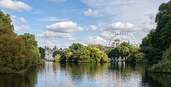 Photograph looking east over St. James's Park Lake from the Blue Bridge, with the London Eye and parks of White Hall visible above the trees in the distance.