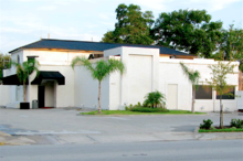 A street-level view of a small white structure with a blue roof, black awnings, and empty parking lot