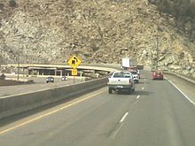 A sharp curve with a cut in the mountain visible to support the highway