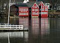 Three bright red buildings stand across the river from the photographer; one of them has a sign saying "Lowell's Boat Shop".