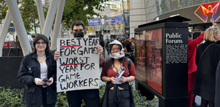 Three protestors, one holding a sign that reads "best year for games worst year for game workers"
