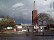 A brown-bricked building with a rectangular, dark blue sign reading "OSTERLEY STATION" in white letters all under a dark sky with white clouds