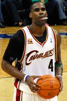 A basketball player wearing a white jersey while chewing his mouth piece as he prepares to take a free throw.