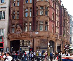 A corner view showing both elevations of a beige terracotta building. The ground floor includes exits from the station and the upper storeys feature a combined brick and terracotta elevation.