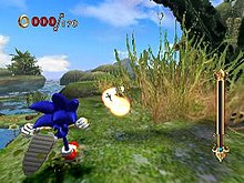 The hedgehog runs up a grassy hill which veers off to the right, partially obscured by a bush. He prepares to run into a trail of bright spheres resembling pearls. The area overlooks a swamp and the deep daytime sky.