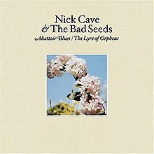 A photograph of a series of flowers in part of an arc are surrounded by a cream coloured border. Black text above the photograph reads "Nick Cave & The Bad Seeds" and italicised black text reads "Abattoir Blues / The Lyre of Orpheus".