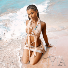 Tyla sitting in the swash on the beach wearing a two-piece outfit and a necklace