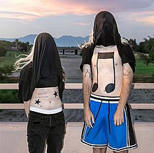 Two people stand with the front of their black shirts pulled over their heads. The exposed midriff on the left has two black stars, and the chest on the right has two musical notes.