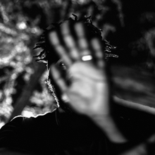 A black-and-white photograph of Clark's blurry hand in front of his in-focus face against an indistinct background