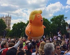 The helium balloon floating outdoors, held by restraining cords, surrounded by protesters, with the Houses of Parliament in the background