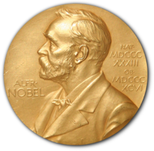 A golden medallion with an embossed image of a bearded man facing left in profile. To the left of the man is the text "ALFR•" then "NOBEL", and on the right, the text (smaller) "NAT•" then "MDCCCXXXIII" above, followed by (smaller) "OB•" then "MDCCCXCVI" below.