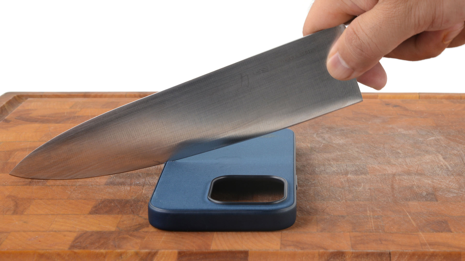 A kitchen knife cutting an iPhone case on a butting board