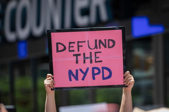 A protester in Times Square holds up a handmade sign that reads, "Defund The NYPD"