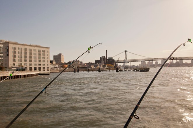 Three fishing rods hanging over a pier along the East River in New York City as the sun sets over the Brooklyn Bridge.