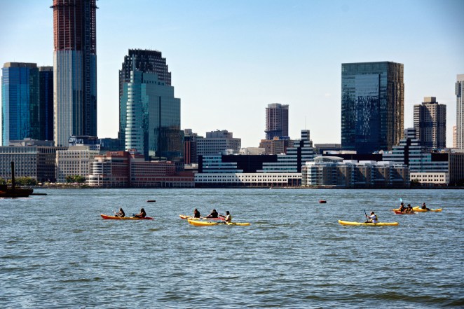 New York City, USA - September 30, 2018: A large group of people are seen Kayaking in the Hudson River just off of Hudson Park in Lower Manhattan. Behind them is a cityscape of skyscrapers in Jersey City, New Jersey.