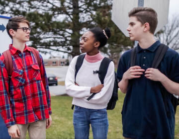 Two teenage boys and a teenage girl talking outside of school