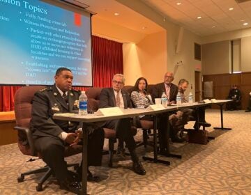 From left, Interim PPD Commissioner John Stanford, District Attorney of Philadelphia Larry Krasner and others participate in a panel, seated at a table, with a slideshow visible behind them.