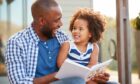 Young black father and daughter reading book outside