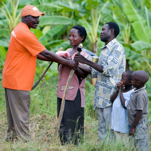World Vision employee hands farming tools to a woman and man with their two children watching.