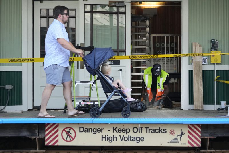 A pedestrian and child walk past a Chicago Transit Authority employee as he makes repairs at the Ashland Ave. station Sunday, Aug. 4, 2024, near the United Center where the Democratic National Convention will convene Monday, August 19, in Chicago. (AP Photo/Charles Rex Arbogast)