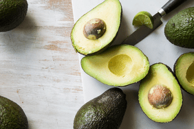 Avocados whole and slices in half on a cutting board with a knife and lime alongside.