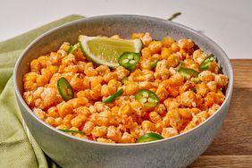 bowl of fried corn kernels dotted with jalapeno slices and lime wedge