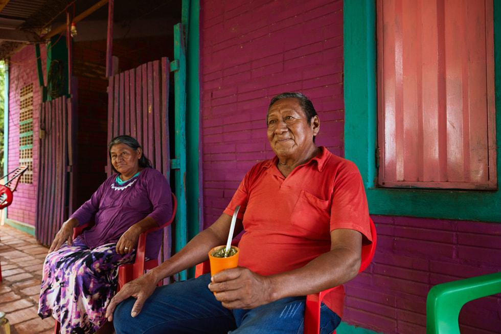 Ramon Mariotti holds a cup of yerba mate while sitting on a porch with a companion.