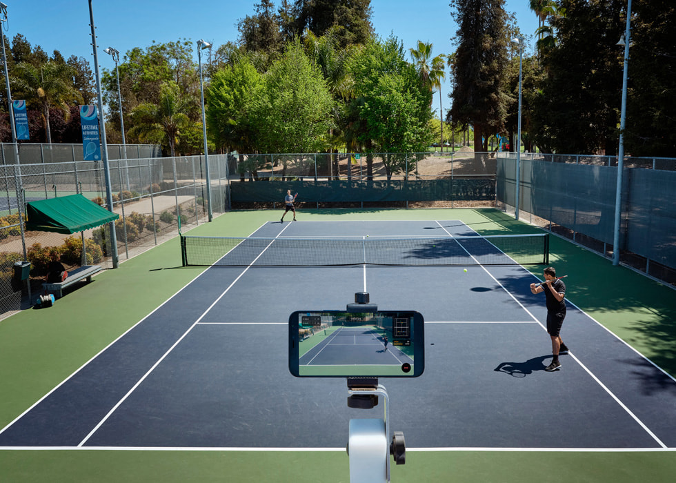 iPhone posicionado para gravar duas pessoas jogando tênis em quadra.