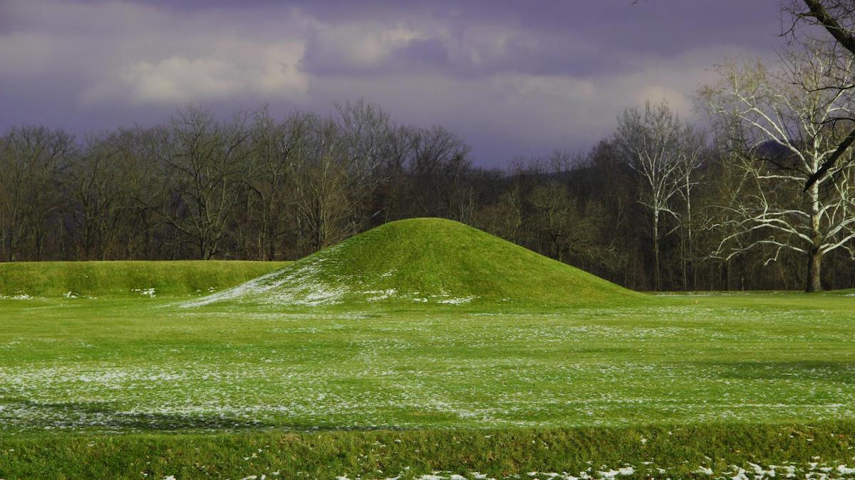 A grassy mound with some snow on its side.