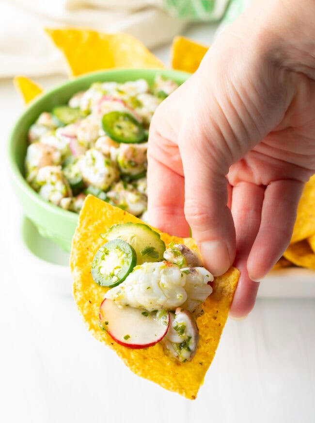 Hand holding tortilla chip loaded with aguachile verde.