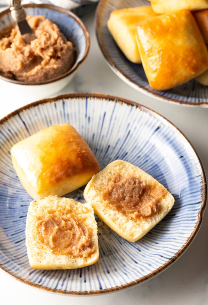 Two yeast rolls on a plate, one roll has been opened and smeard with cinnamon butter.