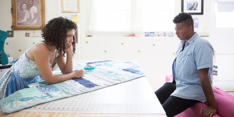 A still from the 36th best lesbian movie of all time Suicide Kale. Jasika Nicole and Brittani Nichols stand across from each other looking serious and leaning on furniture.